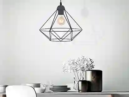 Eine geometrische Lampe hängt über einem gedeckten Tisch mit Geschirr und einer Vase mit Blumen.