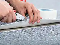 Eine Person schneidet mit einem Teppichmesser einen Teppich zu.