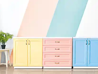 Drei bunte Schränke stehen nebeneinander vor einer Wand mit diagonalen Pastellstreifen.
