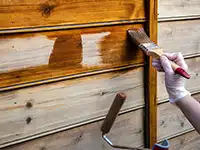 Eine Person streicht eine Holzfläche mit einem Pinsel, um sie zu versiegeln.