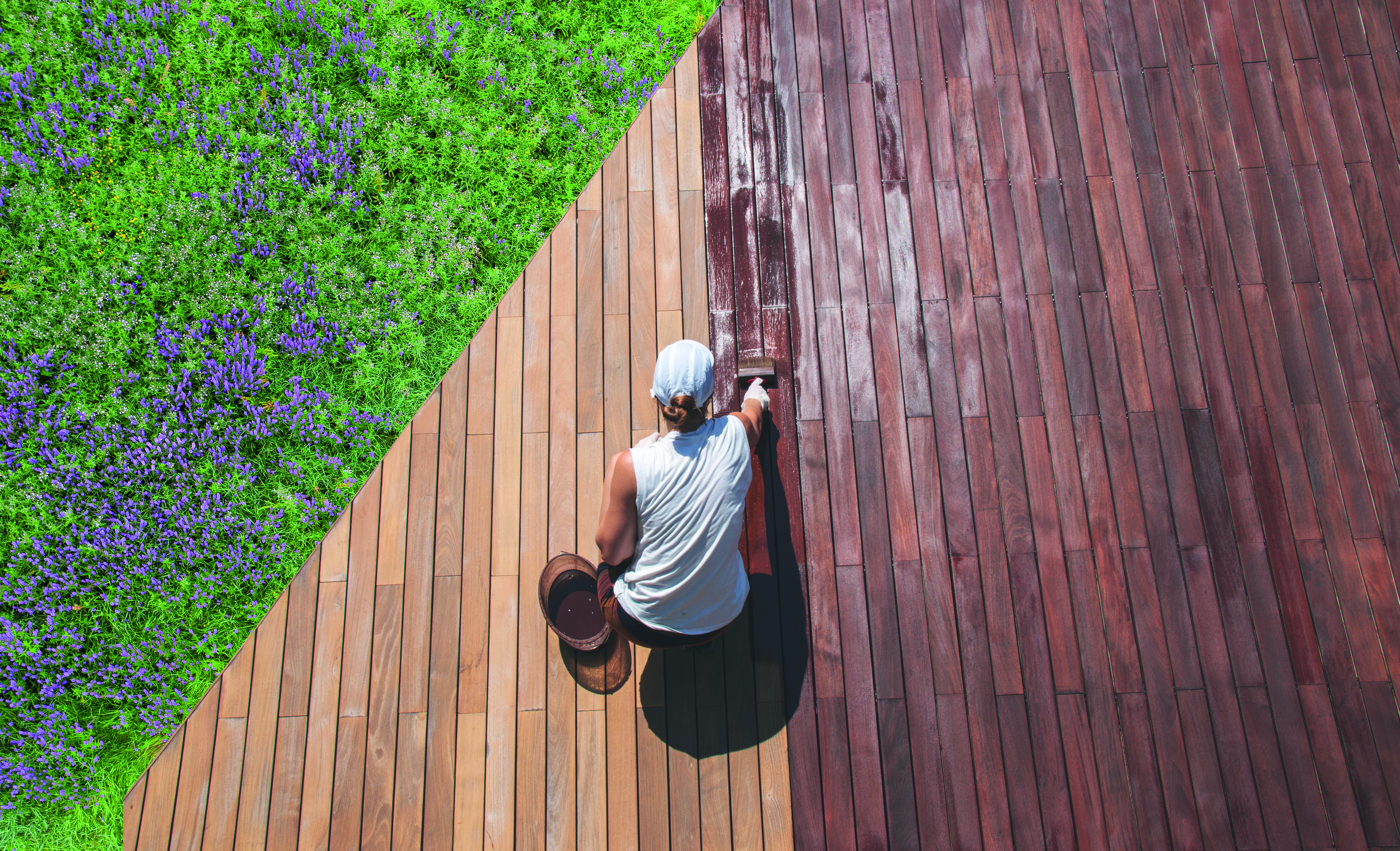 Mann der eine Holzterrasse streicht