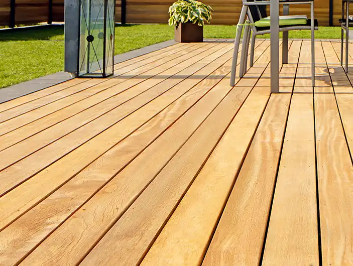 Eine Holzterrasse mit Tisch und Stühlen steht in einem Garten mit grünem Rasen.