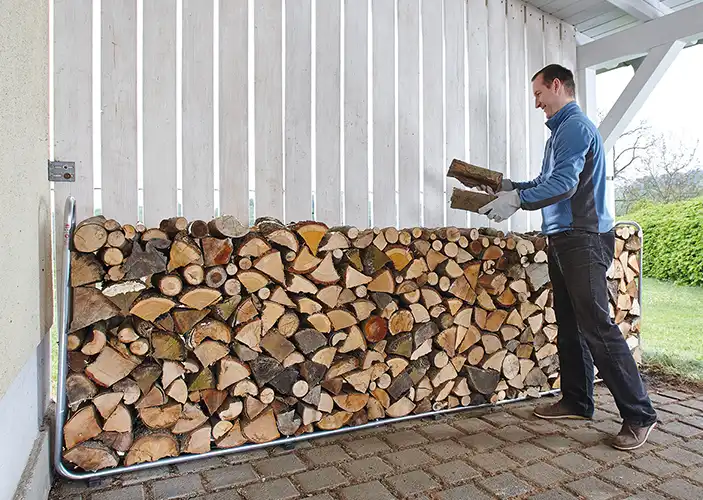 Mann stapelt Holz an einer weißen Holzwand