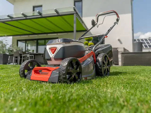 Rasenmäher auf Rasenfläche vor Terrasse mit grüner Überdachung