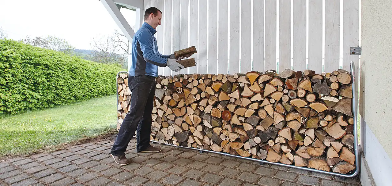Mann stapelt Holz an einer weißen Holzwand