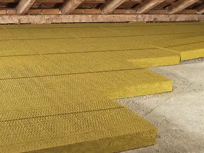 Gelbe Dämmplatten liegen gleichmäßig auf einem Dachbodenboden unter freiliegenden Dachbalken.