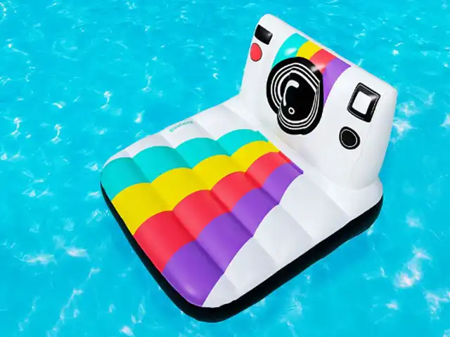 Eine bunte, kameraförmige Schwimmluftmatratze treibt auf klarem, blauem Wasser.