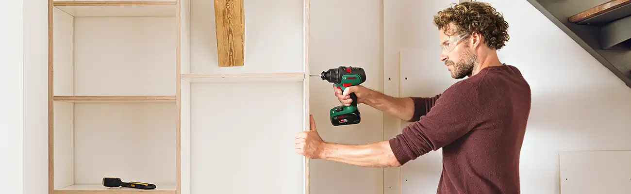 Ein Mann benutzt einen Akkubohrer, um ein Holzregal zu bauen.