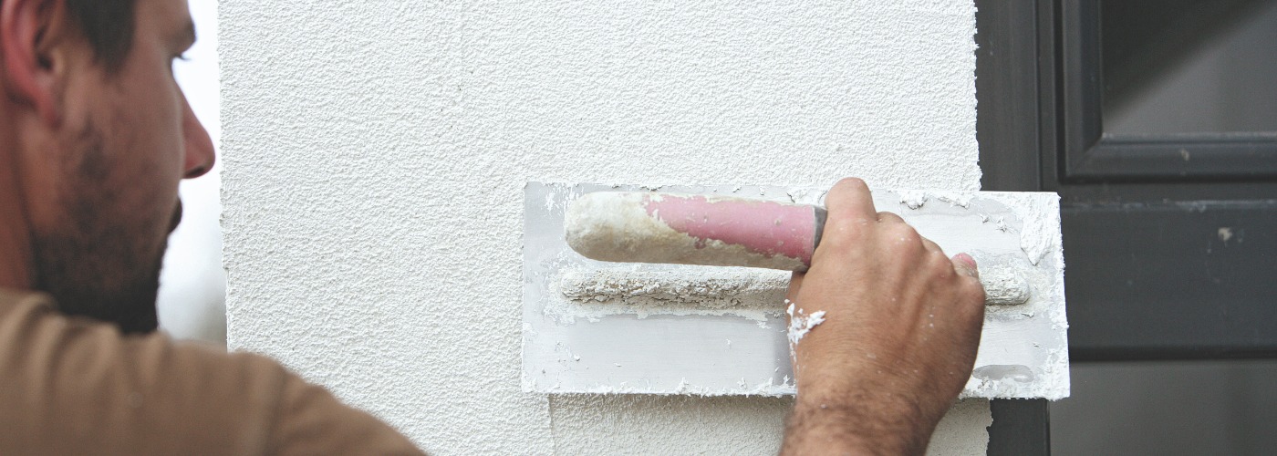 Ein Mann der eine Außenwand neben der Tür verputzt