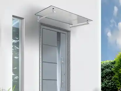 Eine moderne Haustür mit Glasvordach befindet sich an einer weißen Wand neben einem Fenster.